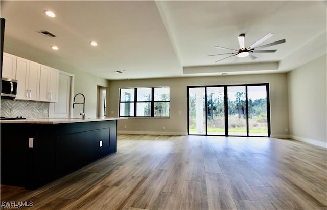 kitchen with white cabinets, sink, a raised ceiling, light wood-type flooring, and ceiling fan