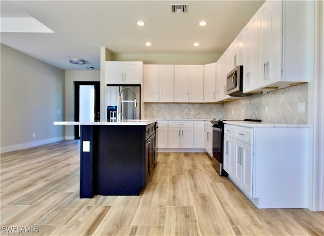 kitchen with sink, a kitchen island with sink, tasteful backsplash, white cabinets, and light wood-type flooring