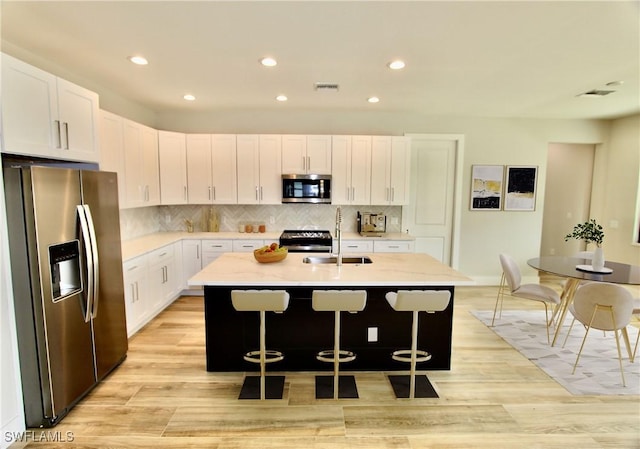 kitchen with white cabinetry, stainless steel appliances, a kitchen island with sink, light stone counters, and a breakfast bar