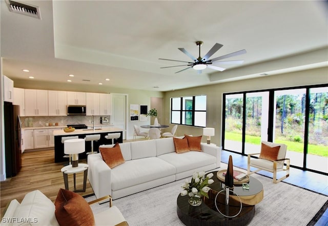 living room featuring light wood-type flooring, ceiling fan, and sink