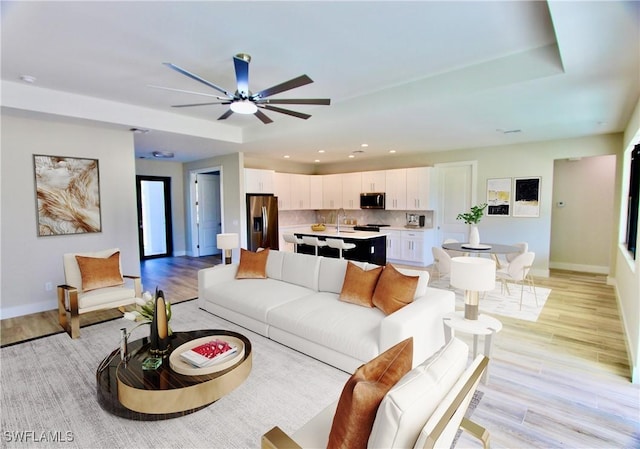 living room featuring a raised ceiling, ceiling fan, sink, and light hardwood / wood-style floors