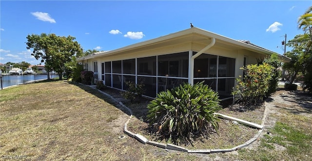 view of side of property with a sunroom, a lawn, and a water view