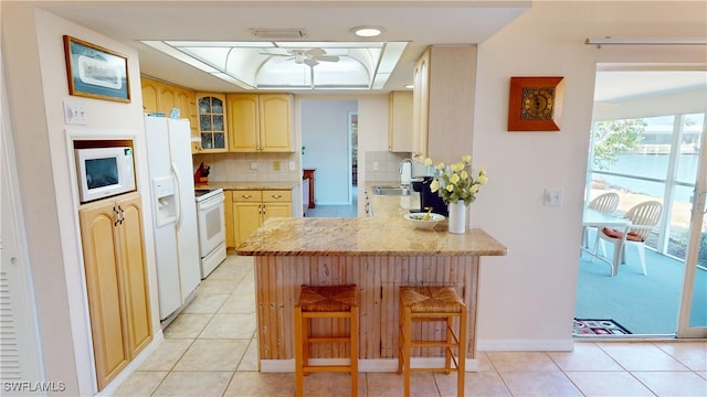 kitchen with kitchen peninsula, tasteful backsplash, white appliances, light brown cabinetry, and sink