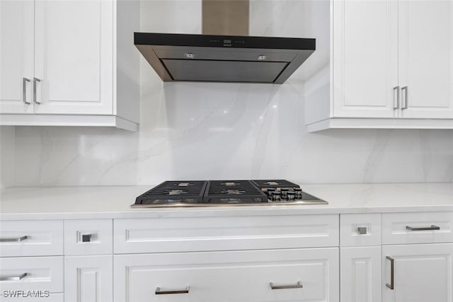 kitchen featuring backsplash, wall chimney exhaust hood, light stone countertops, white cabinets, and stainless steel gas stovetop