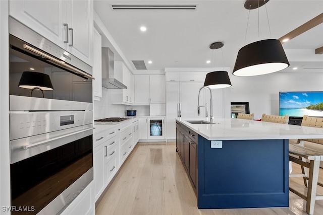 kitchen with a sink, wall chimney exhaust hood, white cabinets, light wood finished floors, and light countertops