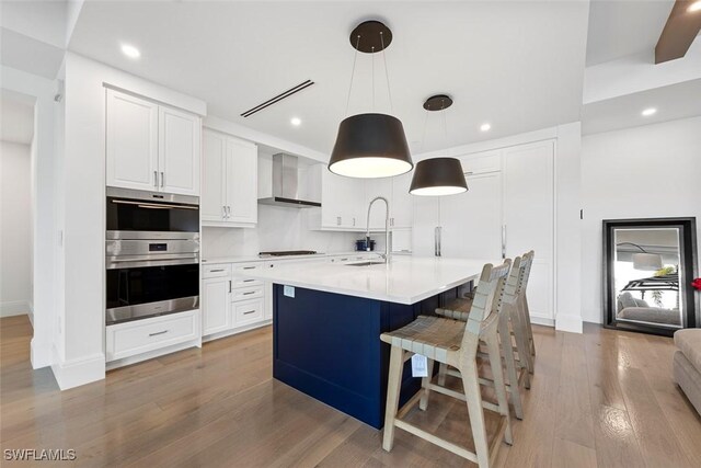 kitchen featuring stovetop, light wood-style floors, double oven, wall chimney exhaust hood, and light countertops