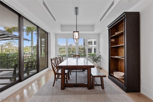 dining room with a raised ceiling, baseboards, visible vents, and light wood-type flooring