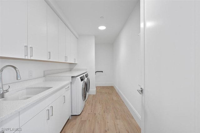 clothes washing area featuring cabinets, washing machine and clothes dryer, light hardwood / wood-style floors, and sink