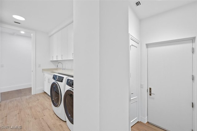 laundry area featuring washer and dryer, visible vents, cabinet space, and light wood-style flooring