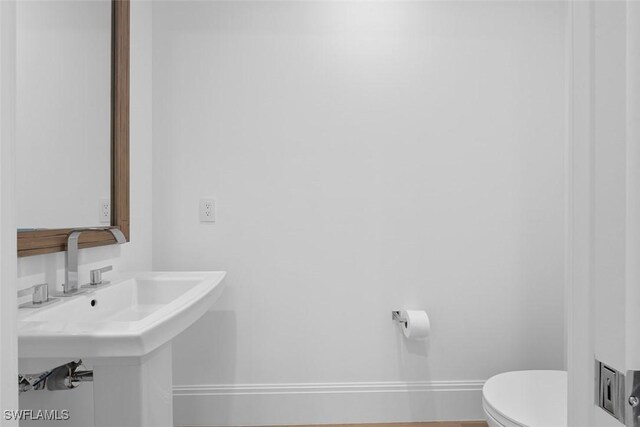 half bathroom with toilet, baseboards, and a sink