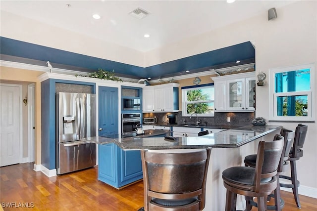 kitchen with appliances with stainless steel finishes, white cabinetry, a kitchen breakfast bar, light wood-type flooring, and blue cabinets