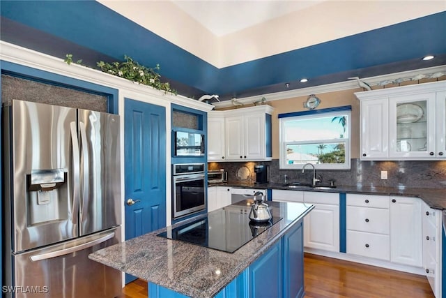 kitchen with white cabinetry, stainless steel appliances, dark stone countertops, a kitchen island, and sink