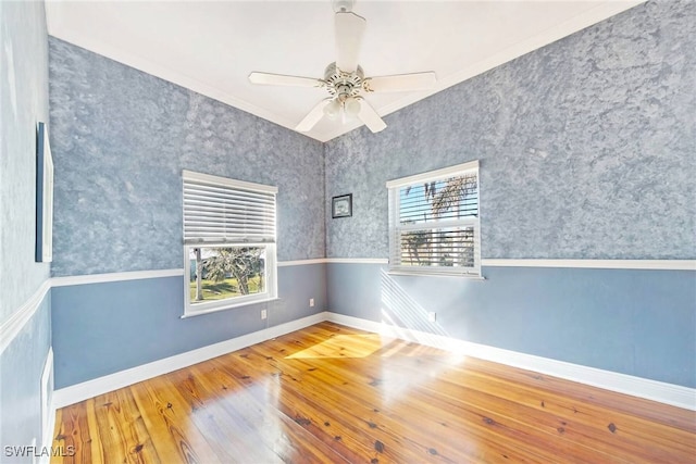 empty room featuring ceiling fan, wood-type flooring, a wealth of natural light, and crown molding