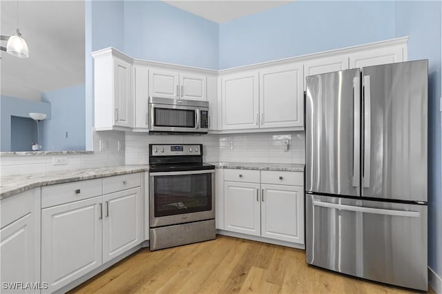 kitchen with white cabinetry, backsplash, hanging light fixtures, light hardwood / wood-style floors, and stainless steel appliances