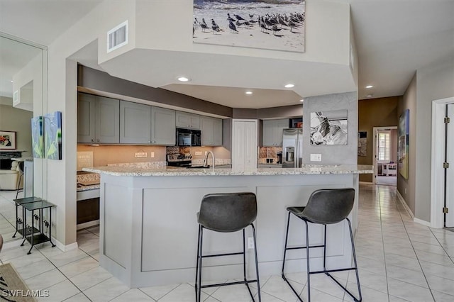 kitchen featuring a kitchen bar, gray cabinetry, light tile patterned floors, and stainless steel appliances