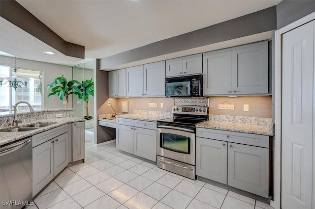 kitchen with sink, stainless steel appliances, light stone counters, and gray cabinetry