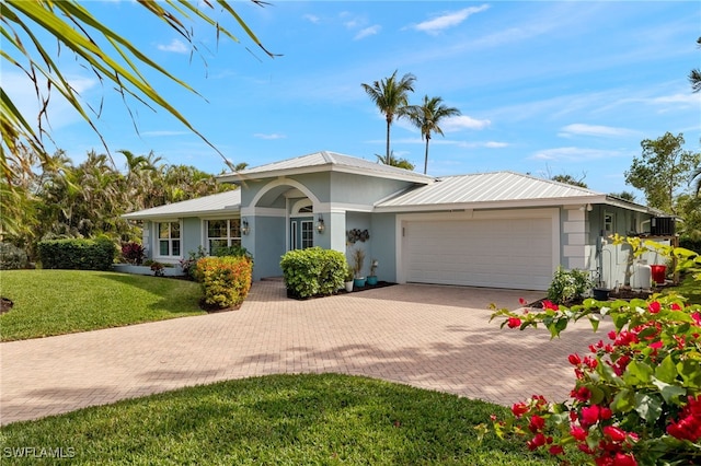 single story home with metal roof, an attached garage, decorative driveway, stucco siding, and a front yard