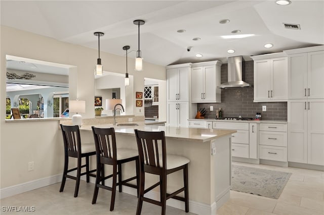 kitchen featuring lofted ceiling, white cabinets, a sink, and wall chimney exhaust hood