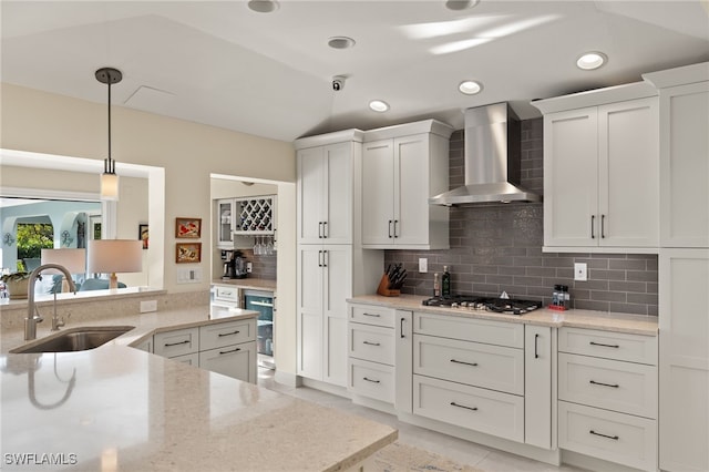 kitchen featuring white cabinets, light stone countertops, wall chimney range hood, pendant lighting, and a sink