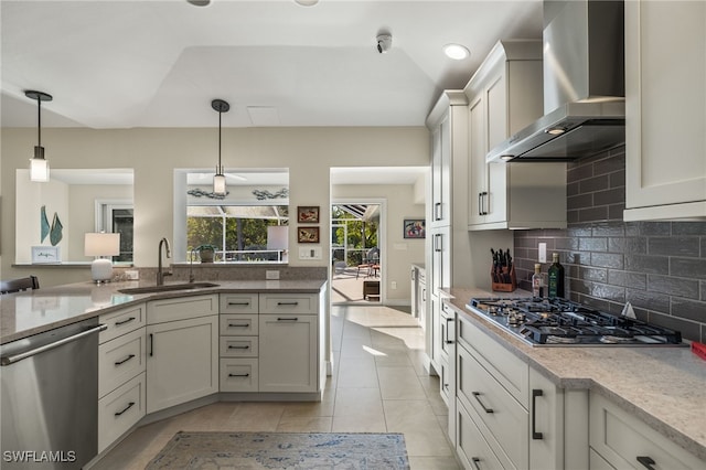 kitchen featuring wall chimney exhaust hood, appliances with stainless steel finishes, a sink, and decorative light fixtures