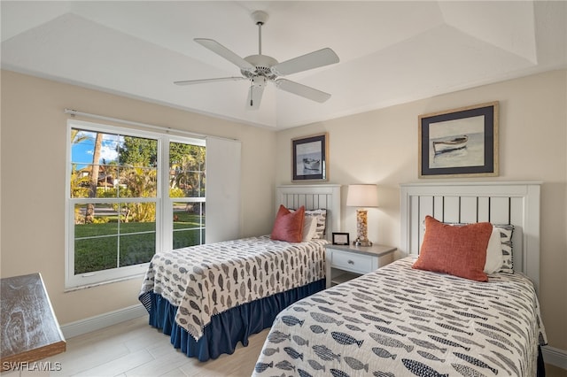 bedroom featuring ceiling fan, light wood-style flooring, baseboards, and a raised ceiling