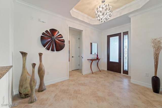 foyer entrance with ornamental molding, a tray ceiling, and a notable chandelier