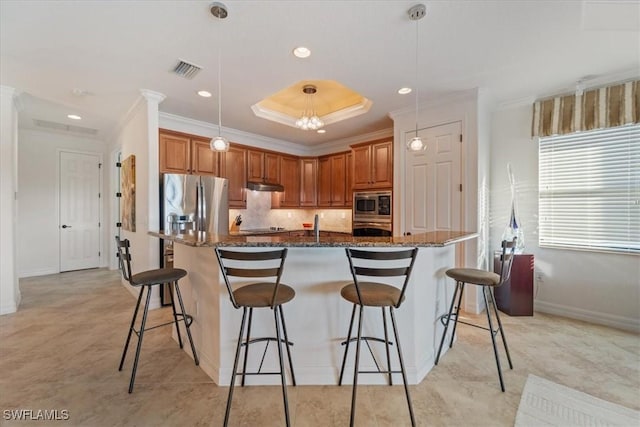 kitchen with a breakfast bar, hanging light fixtures, stainless steel appliances, a tray ceiling, and a center island with sink