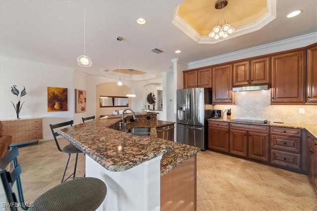 kitchen featuring stainless steel appliances, an island with sink, hanging light fixtures, and a raised ceiling