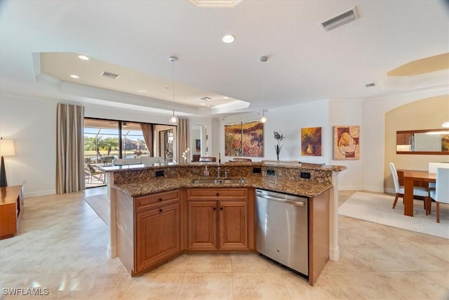 kitchen with a raised ceiling, dishwasher, sink, and an island with sink