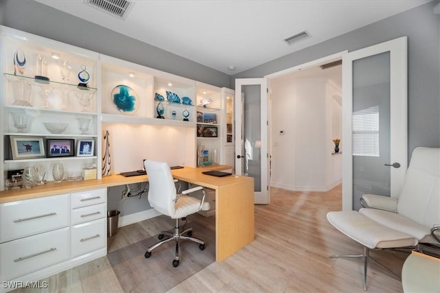 home office with built in desk and light hardwood / wood-style flooring