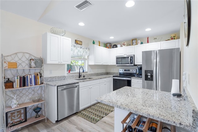 kitchen featuring appliances with stainless steel finishes, light stone countertops, white cabinets, a breakfast bar, and sink