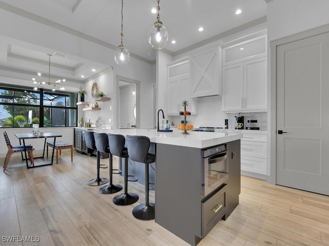 kitchen with hanging light fixtures, a center island with sink, and white cabinets