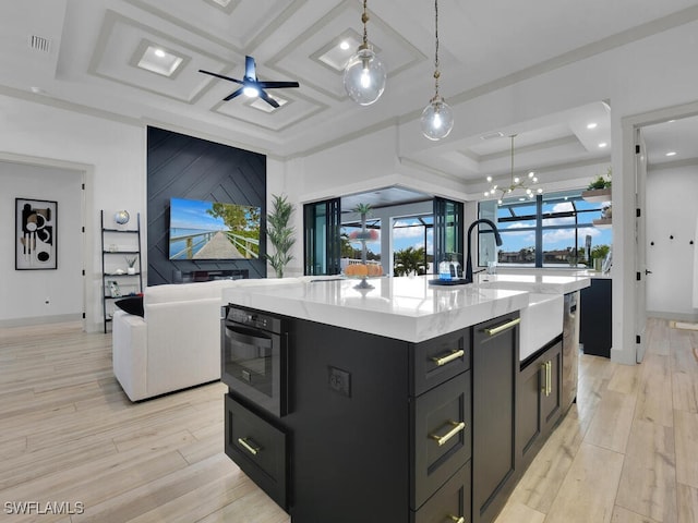 kitchen with pendant lighting, coffered ceiling, a center island with sink, and light wood-type flooring