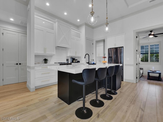 kitchen with white cabinetry, decorative light fixtures, light hardwood / wood-style floors, and an island with sink