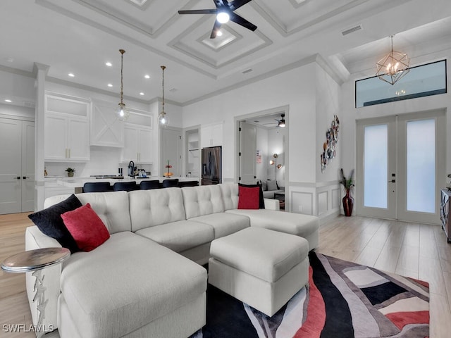 living room featuring french doors, coffered ceiling, light wood-type flooring, ornamental molding, and ceiling fan with notable chandelier