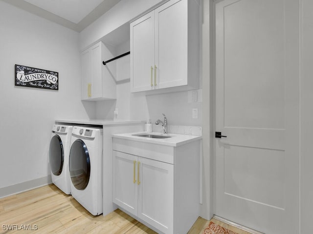 washroom featuring cabinets, sink, washing machine and clothes dryer, and light hardwood / wood-style floors