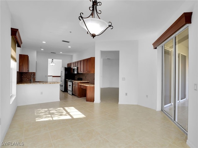 kitchen featuring light tile patterned flooring, kitchen peninsula, stainless steel appliances, light stone countertops, and decorative backsplash