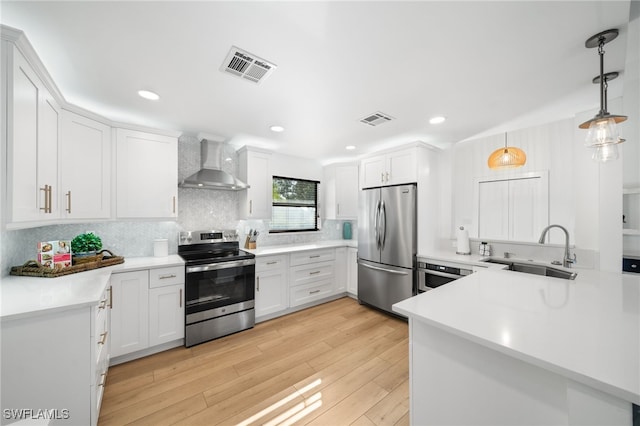 kitchen featuring pendant lighting, wall chimney range hood, sink, white cabinetry, and stainless steel appliances