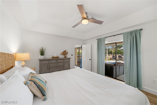 bedroom featuring light hardwood / wood-style flooring, a tray ceiling, access to outside, and ceiling fan