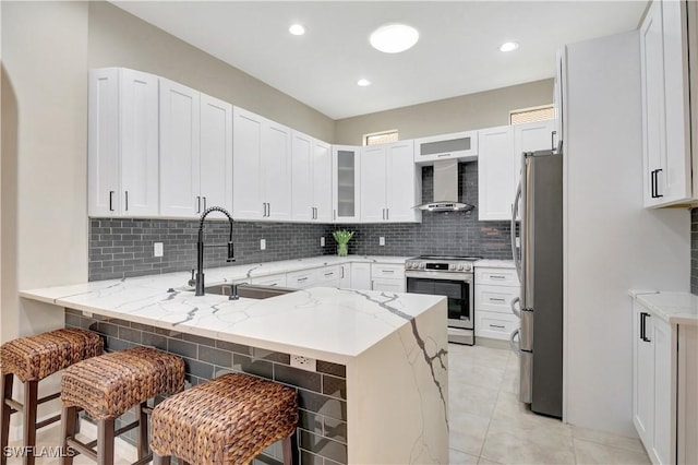 kitchen featuring wall chimney range hood, a breakfast bar, kitchen peninsula, sink, and stainless steel appliances