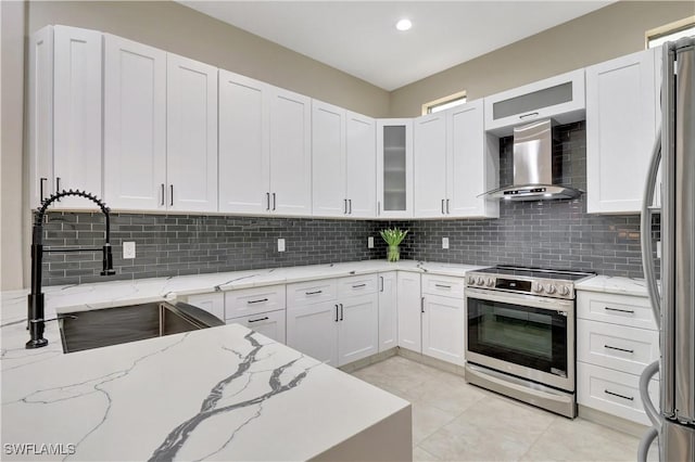 kitchen with stainless steel appliances, white cabinets, light stone counters, and wall chimney range hood