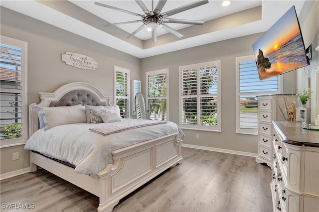 bedroom with ceiling fan, light hardwood / wood-style floors, and a tray ceiling