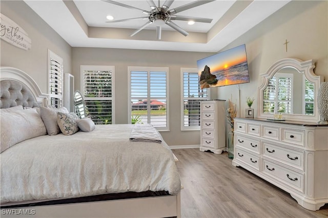 bedroom with ceiling fan, a raised ceiling, and light wood-type flooring