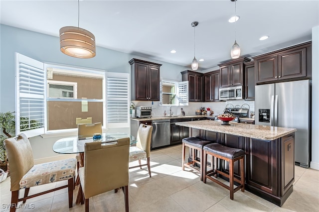 kitchen with pendant lighting, light tile patterned floors, stainless steel appliances, light stone countertops, and a kitchen island