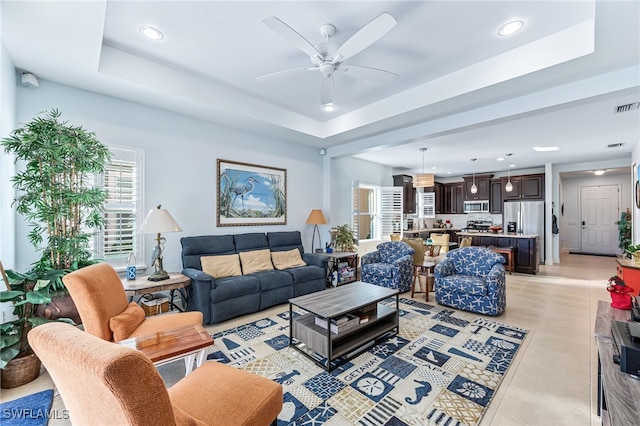 living room featuring light tile patterned flooring, ceiling fan, and a tray ceiling