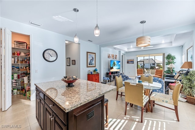 kitchen with light stone countertops, dark brown cabinets, pendant lighting, and a tray ceiling