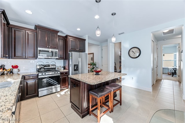 kitchen with stainless steel appliances, dark brown cabinetry, light stone counters, a kitchen island, and decorative light fixtures