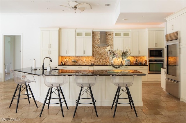 kitchen with a large island with sink, a kitchen bar, tasteful backsplash, and built in appliances