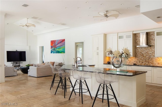 kitchen featuring a breakfast bar, white cabinetry, wall chimney range hood, and a large island