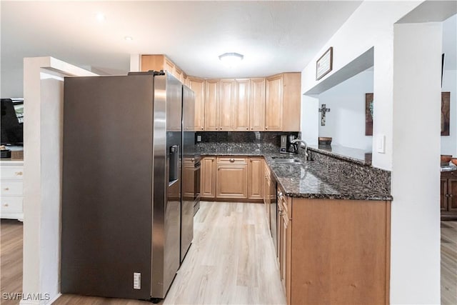 kitchen with stainless steel refrigerator with ice dispenser, backsplash, light wood-type flooring, dark stone countertops, and sink